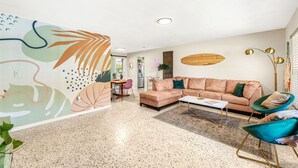 A modern living room with a sofa, chairs, a coffee table, and a decorative wall mural. - Villa Oasis • 1 Block to Beach + Downtown Cocoa Beach (Cocoa Beach)