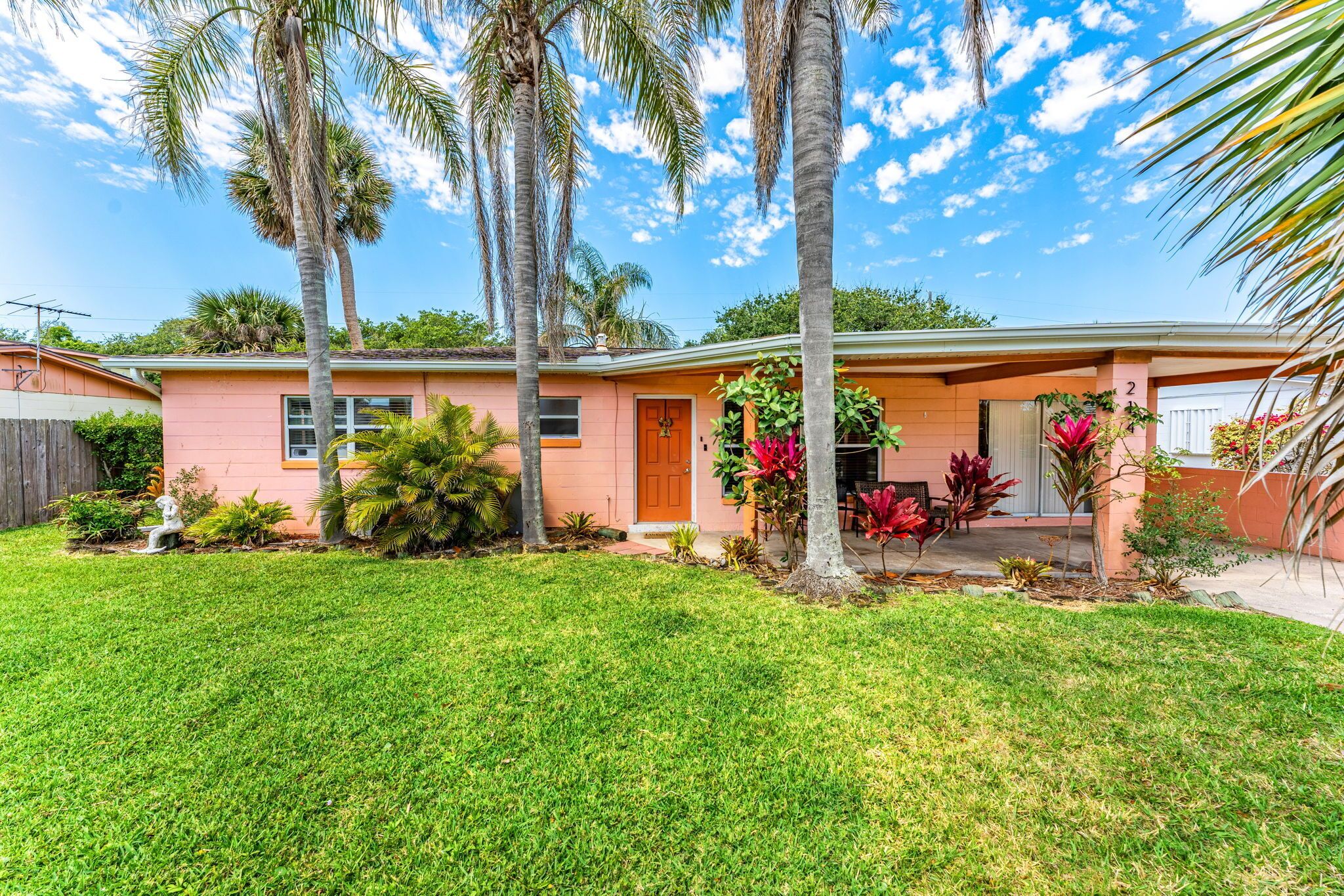 A single-story house with a pink exterior, a front porch, and a well-maintained lawn.