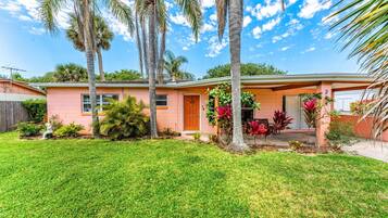 A single-story house with a pink exterior, a front porch, and a well-maintained lawn.