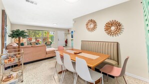 A dining area with a wooden table, white chairs, a bench, and decorative wall art. - Villa Oasis • 1 Block to Beach + Downtown Cocoa Beach (Cocoa Beach)