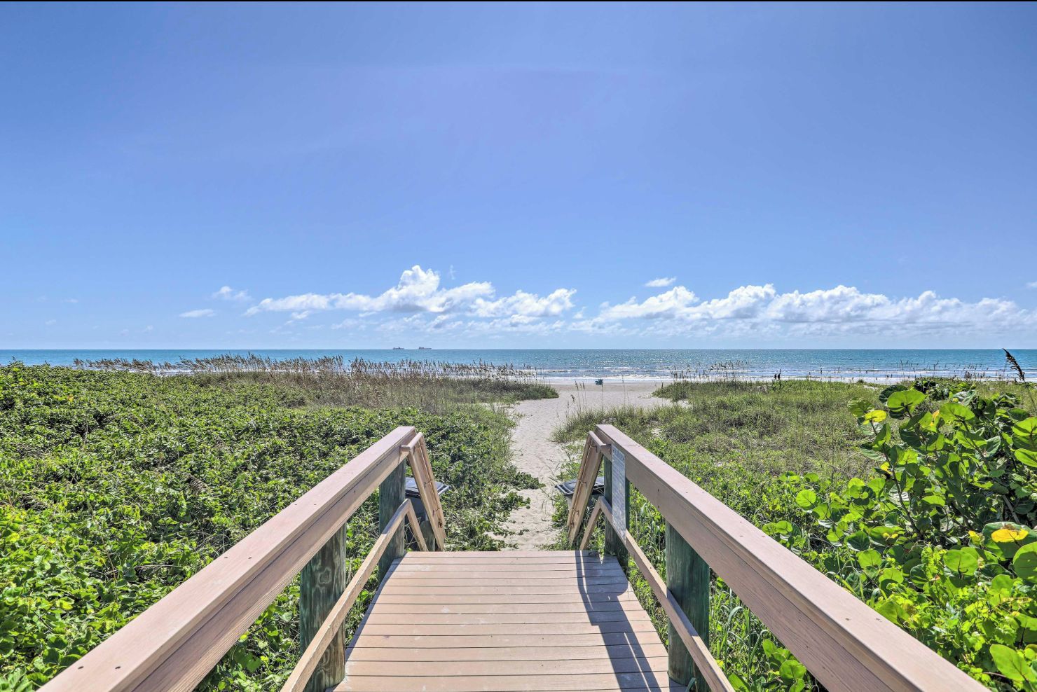 A wooden boardwalk leading to a beach with a clear sky.
