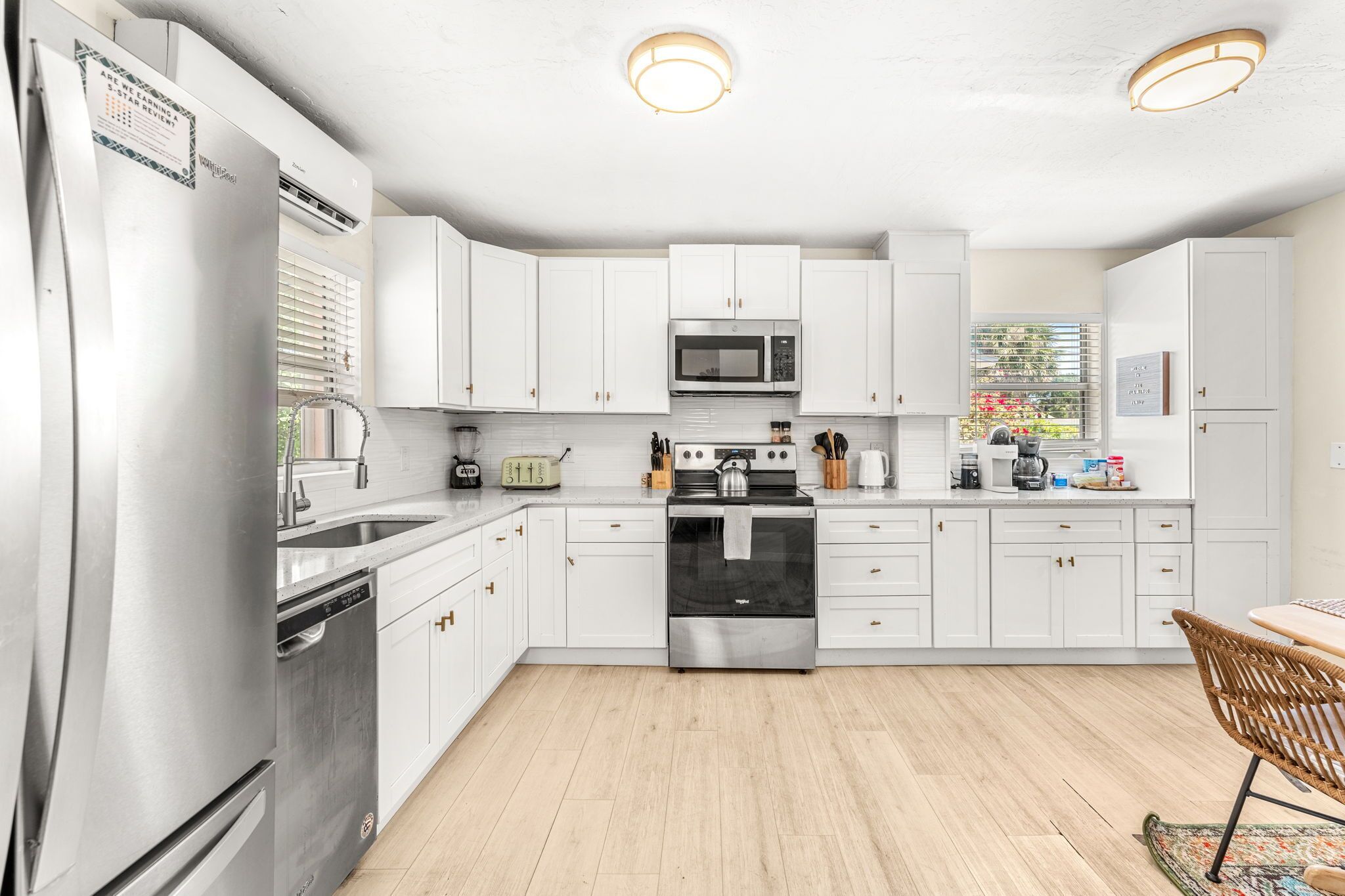 A modern kitchen with white cabinets, stainless steel appliances, and a wooden floor.