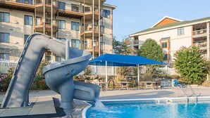 Une piscine dotée d’un élément aquatique original, entourée d’un bâtiment agrémenté de balcons et d’un patio couvert.