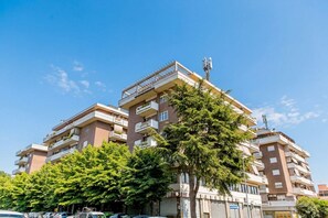 Un immeuble résidentiel à plusieurs étages, doté de balcons, avec un ciel dégagé et des voitures garées.