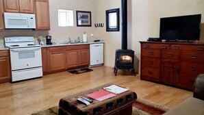 Eine Küche mit Herd, Mikrowelle und Geschirrspüler, ein Wohnzimmer mit Fernseher und Kamin sowie ein Couchtisch mit Büchern und Fernbedienungen.
