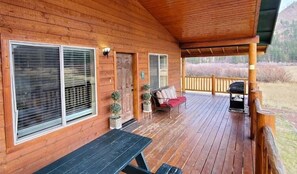 Eine Holzhütte mit Veranda, einer Bank, einem Tisch und einem Grill.