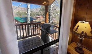 A balcony with a grill, a lamp, and a view of a house and trees.