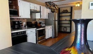 A compact kitchen with white cabinets, a stove, a refrigerator, and a coffee maker.