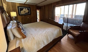 A room with a large bed, a chair, a framed picture, and a window.