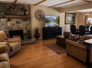 A living room with a stone fireplace, leather sofas, a TV, and a dining area with chairs and a table.