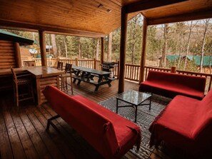 A covered outdoor area with wooden furniture, a grill, and a view of trees.