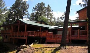 A cabin with a covered porch, a fenced deck, and a wooded backdrop.