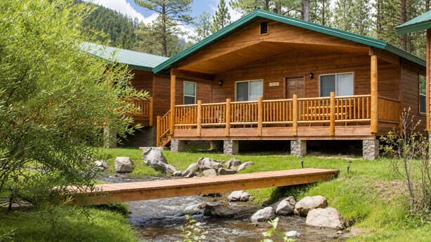Eine Holzhütte mit einer Veranda, einem kleinen Bach und einer Brücke.