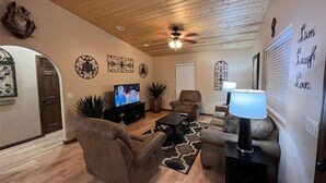 Ein Wohnzimmer mit Fernseher, zwei Sofas, einem Couchtisch, Wanddekoration und einem Deckenventilator.