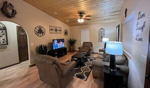 Ein Wohnzimmer mit Fernseher, zwei Sofas, einem Couchtisch, Wanddekoration und einem Deckenventilator.