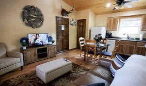 Ein Wohnzimmer mit Fernseher, einer Couch, einem Couchtisch und einem Essbereich mit Stühlen und Tisch.
