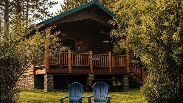 Una cabaña con terraza, dos sillas Adirondack y un estanque.