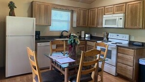 Una cocina compacta con armarios de madera, un refrigerador, un microondas y una mesa de comedor con sillas.
