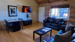 Interior acogedor de una cabaña de madera con comedor, sofá y televisor.