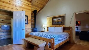 Un dormitorio de cabaña de madera con una cama, un banco, una puerta y un cuadro en la pared.