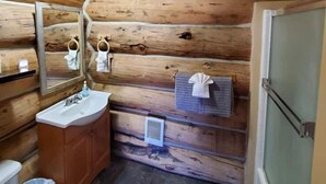 Baño de cabaña de madera con lavamanos, espejo, perchero y ducha.