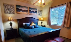 Ein Schlafzimmer mit einem Bett, zwei Nachttischen, einem Deckenventilator und Kunstwerken an den Wänden.