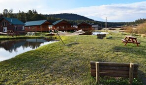 Ein See mit Holzhütten, einer Hängematte, Picknicktischen und einer Bank.