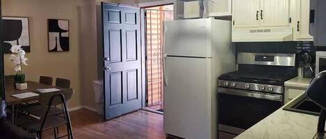 A compact kitchen with a refrigerator, stove, and white cabinets.