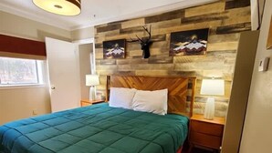 Un dormitorio con cabecera de madera, cubrecama verde, dos mesitas de noche con lámparas y una obra de arte en la pared.