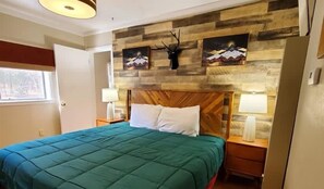 A bedroom with a wooden headboard, a green bedspread, two bedside tables with lamps, and artwork on the wall.