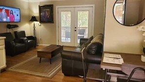 Una sala de estar con sofá, mesa de centro, televisor y puerta con vistas.