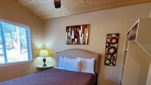Un dormitorio con cama, mesita de noche con lámpara, ventana y una pared decorada con obras de arte.