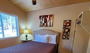 A bedroom with a bed, a nightstand with a lamp, a window, and a wall with artwork. - Tranquil Springs Escape #94 (Greer)