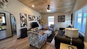 Una sala de estar con televisión, sofá, sillón y decoración mural.