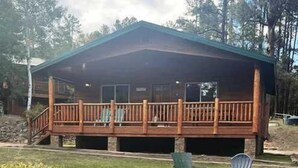 Una cabaña con terraza, mobiliario exterior y vistas al bosque circundante.