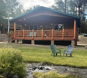 A cabin with a deck, outdoor seating, and a view of the surrounding forest. - Tranquil Springs Escape #94 (Greer)