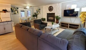 Ein Wohnzimmer mit Sofa, Sessel, Couchtisch, Kamin, Fernseher und einem Essbereich mit Stühlen und Tisch.