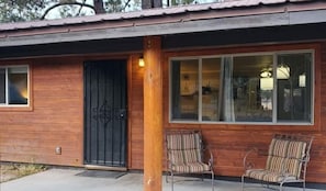 Eine Holzhütte mit einer schwarzen Tür, zwei gestreiften Stühlen und einem Fenster mit Vorhängen.