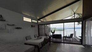 A modern dining area with a table and chairs, a hanging chair, and a view of a body of water through large glass doors. - Lake view Cattle Ranch Villa (Río Chiquito)