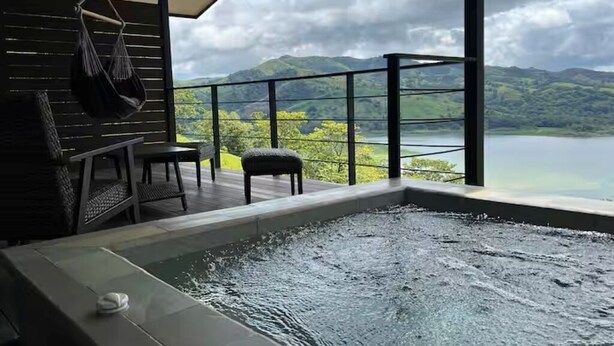 A hot tub with a view of a lake and mountains, a hanging chair, and a table with chairs. - Lake view Cattle Ranch Villa (Río Chiquito)