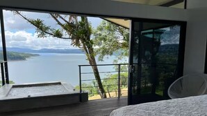 A bedroom with a large bed, a view of a lake, and a balcony with a water feature. - Lake view Cattle Ranch Villa (Río Chiquito)