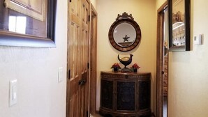 Een gang met een houten deur, een spiegel met sterdecoratie, en een donker houten console met een decoratief object.