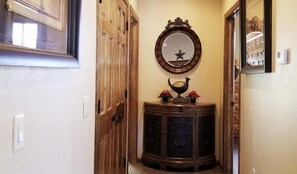 A hallway with a wooden door, a mirror with a star decoration, and a dark wooden console table with a decorative item. - Underwood Lodge #285 (Greer)