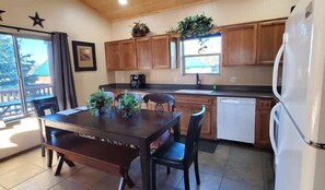 A kitchen with wooden cabinets, a dining table with chairs, a refrigerator, and potted plants. - Underwood Lodge #285 (Greer)