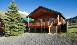 A wooden cabin with a balcony, a gravel driveway, and a large evergreen tree. - Underwood Lodge #285 (Greer)