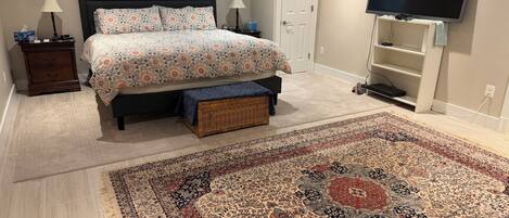Un dormitorio con cama, mesitas de noche, televisor, puerta y alfombra estampada.