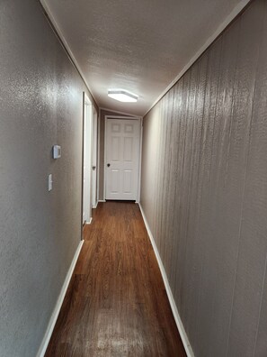 Ein Korridor mit Holzboden, einer weißen Tür am Ende und einer strukturierten Wand an der Seite.