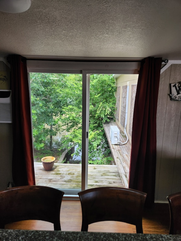 Ein Zimmer mit einer Schiebetür zu einem Balkon mit Blick auf Grünflächen. Im Zimmer befinden sich ein Holztisch und Stühle.