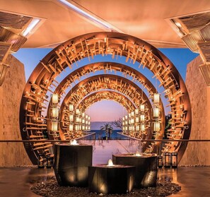 A circular architectural structure with multiple levels of seating and lighting, overlooking a body of water.