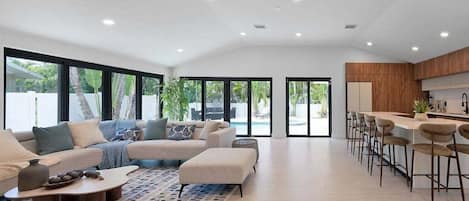 A modern living room with a sofa, coffee table, and a dining area with bar stools.